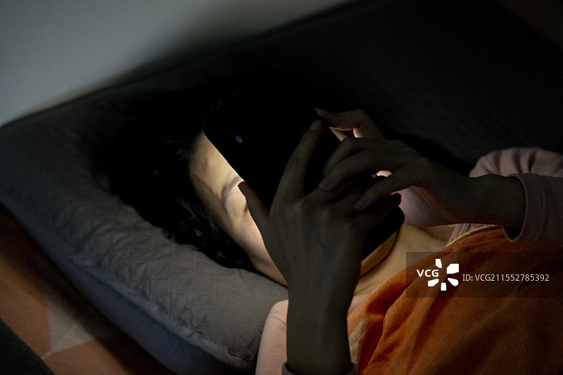 亚洲女士躺床看手机图片素材