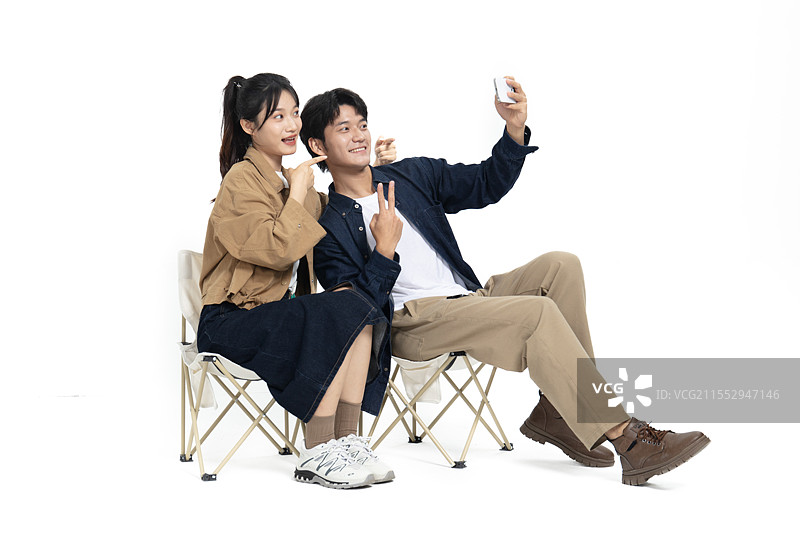 坐在一起户外折叠椅玩自拍的年轻情侣图片素材