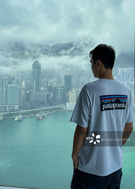 在高楼层落地窗前看云雾中的维多利亚港的男子图片素材