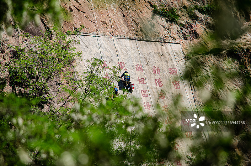 中国山东省泰安市国内著名景点泰山风景区，悬崖上的蜘蛛侠工人正在摩崖石刻上刷漆，户外白昼无人图像摄影图片素材