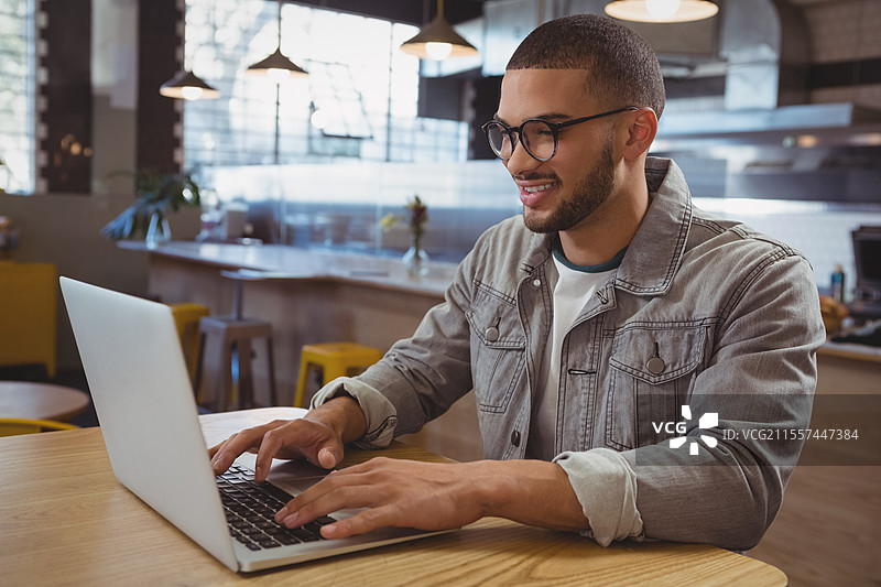 微笑的男子在时尚咖啡馆使用笔记本电脑，享受高效的工作时光图片素材