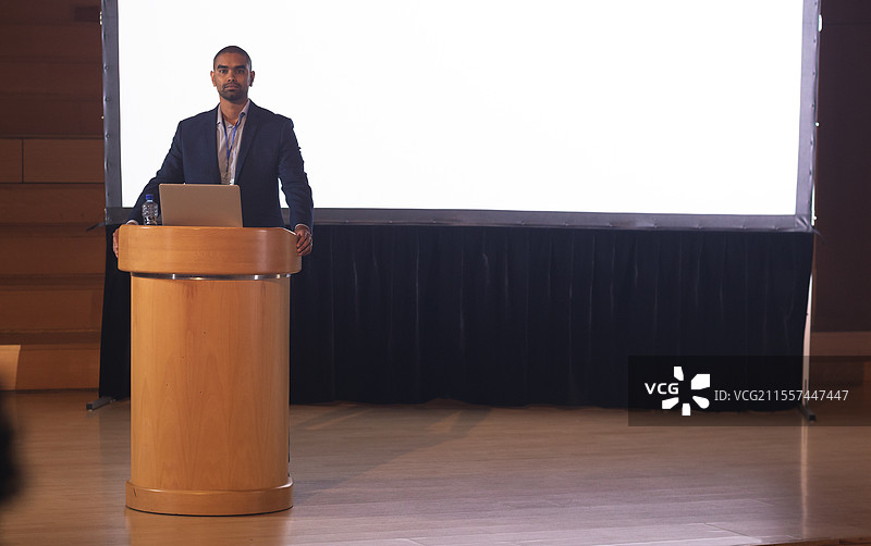 商人在讲台上用笔记本电脑进行演讲，吸引观众注意，留有空白空间图片素材
