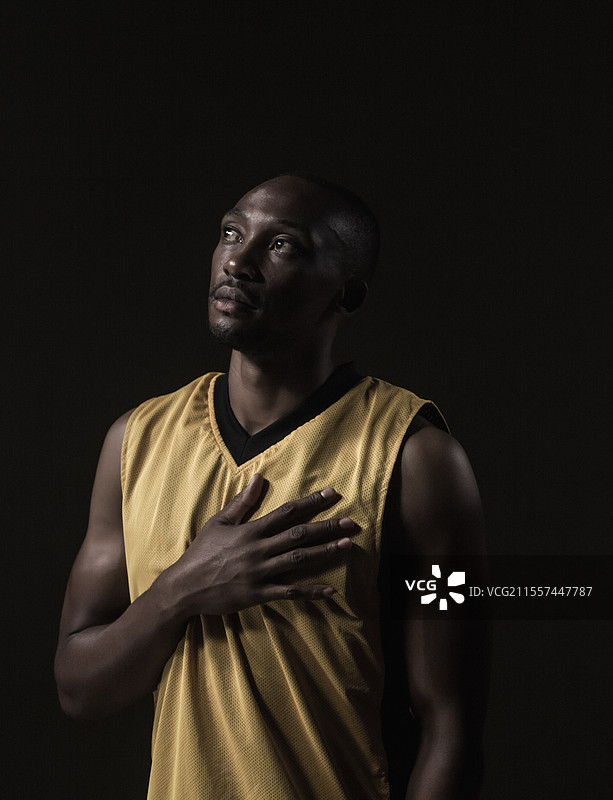 穿着黄色球衣的篮球运动员抬头看，手放在胸前，表情沉思。图片素材