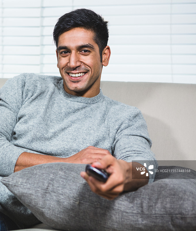 在家沙发上放松的男人，微笑着手握遥控器图片素材