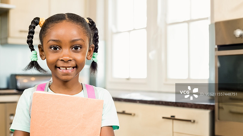 微笑的非裔美国女孩在厨房里拿着书，准备上学，留有空白空间图片素材