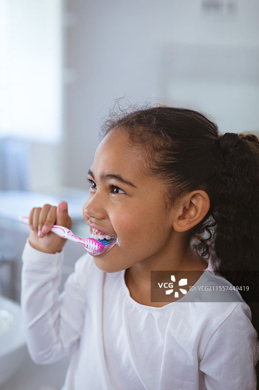 年轻女孩在浴室里用彩色牙刷刷牙，面带微笑，留有空白空间图片素材