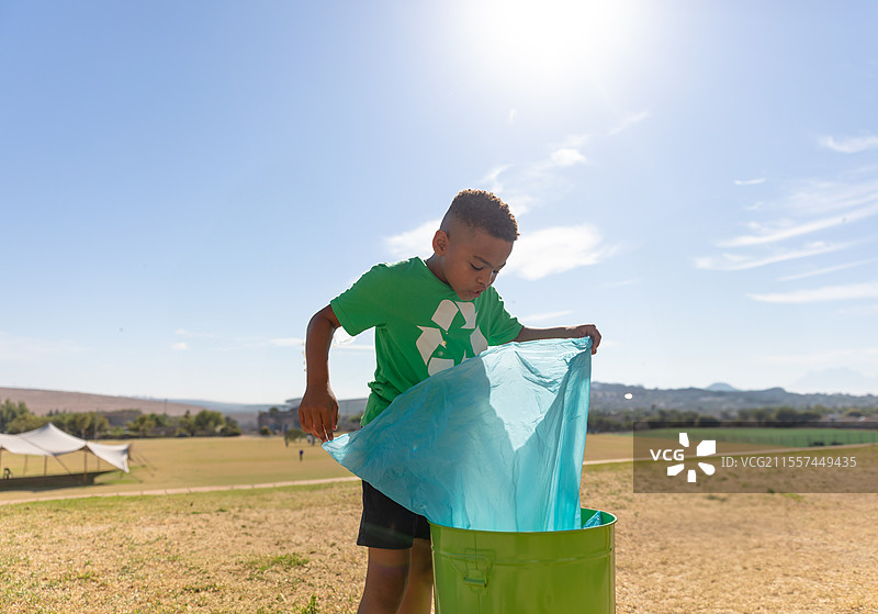穿着绿色衬衫的男孩在户外回收，将塑料袋放入垃圾箱中图片素材