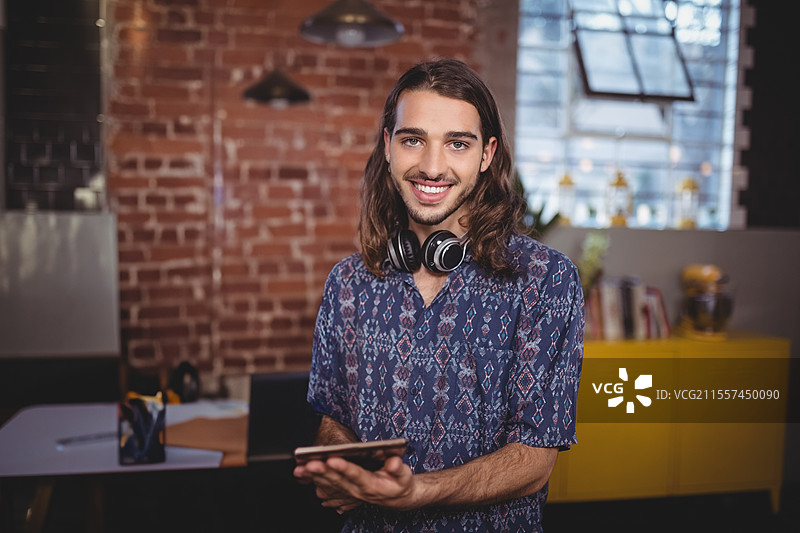 微笑的年轻男子在时尚的城市咖啡馆里戴着耳机使用平板电脑图片素材