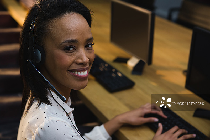 微笑的女性佩戴耳机，在办公桌上打字，留有空白空间图片素材
