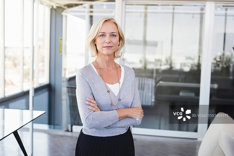 自信的女商人在现代办公室里双臂交叉，神情坚定。图片素材
