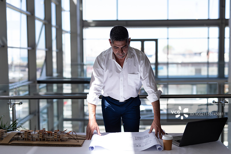 建筑师在办公桌上审查蓝图，旁边有模型和笔记本电脑图片素材