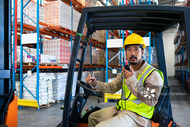 穿着安全装备的仓库工人在操作叉车并通过无线电进行沟通，留白空间图片素材