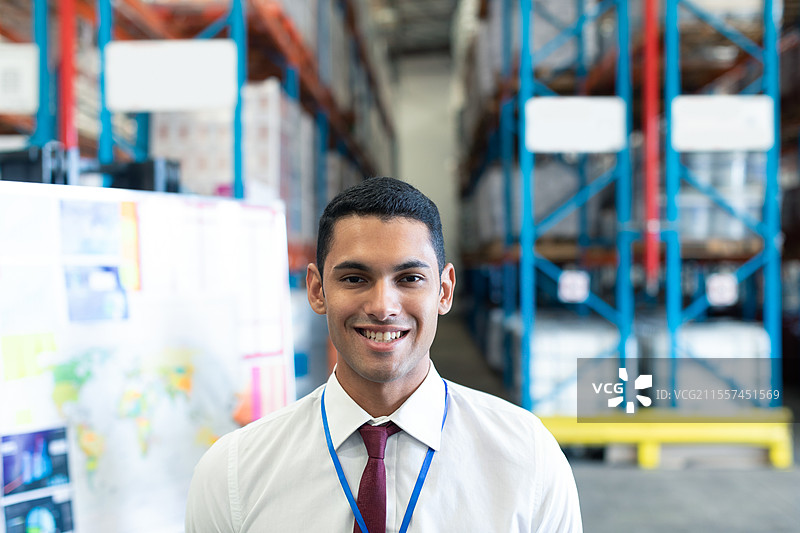 微笑的商人在仓库中自信地站着，背景是货架。图片素材