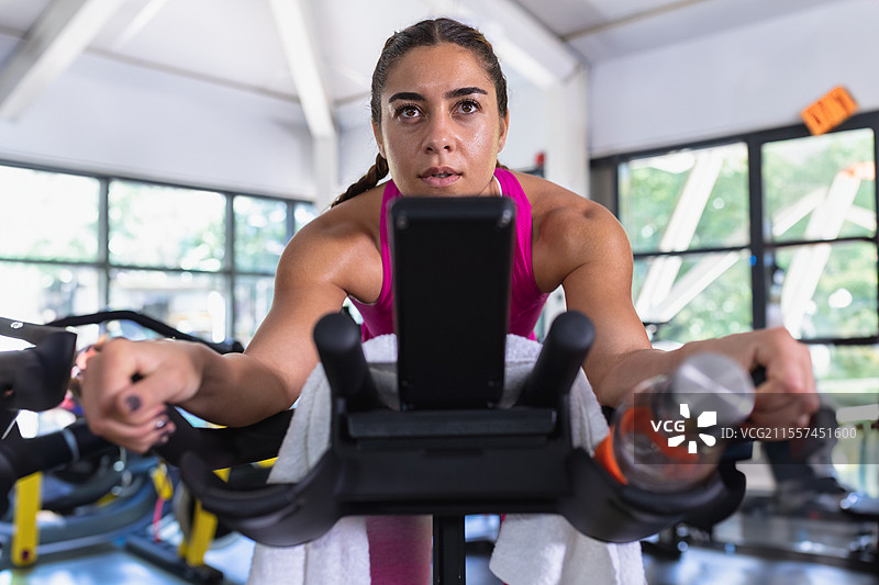专注的女性在健身房骑动感单车，使用智能手机来激励自己图片素材