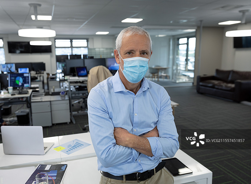 戴着口罩的老年男子在现代办公室环境中自信地站着图片素材