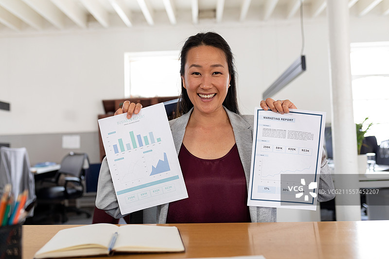 办公室里的一位亚洲女性手持市场报告，自信地对着镜头微笑图片素材