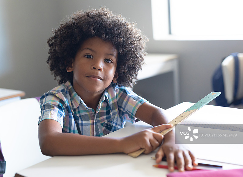 在学校，年轻男孩在桌子上拿着尺子，自信地看着镜头图片素材
