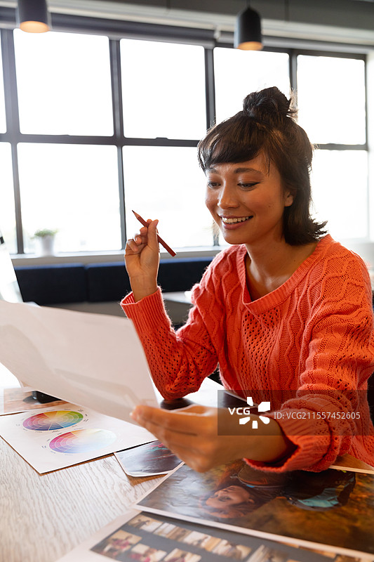 微笑的女性在办公室桌前审阅设计草图，手中拿着红色钢笔图片素材