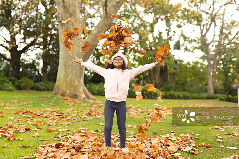 快乐的孩子在公园里玩秋天的落叶，微笑着享受大自然。图片素材