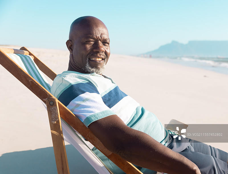 在海滩上放松，老年男子微笑着坐在海边的躺椅上图片素材