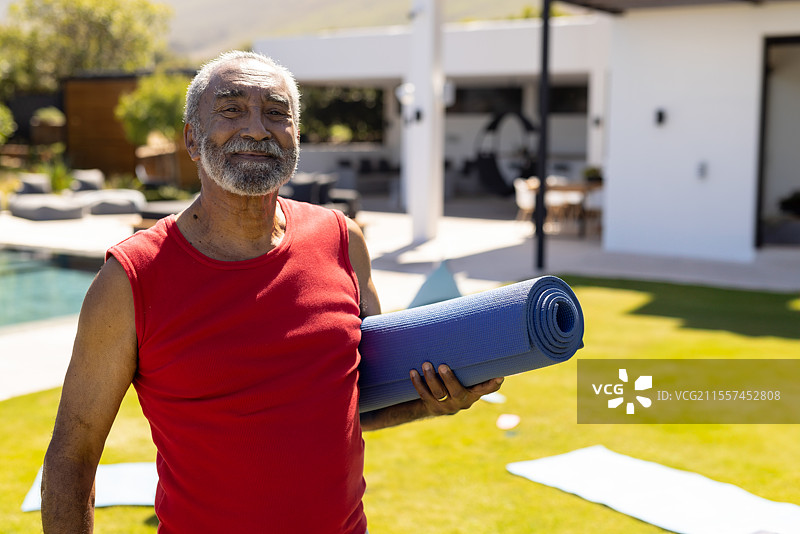 微笑的老年男子在家附近的游泳池旁拿着瑜伽垫，享受阳光，留有空白空间。图片素材
