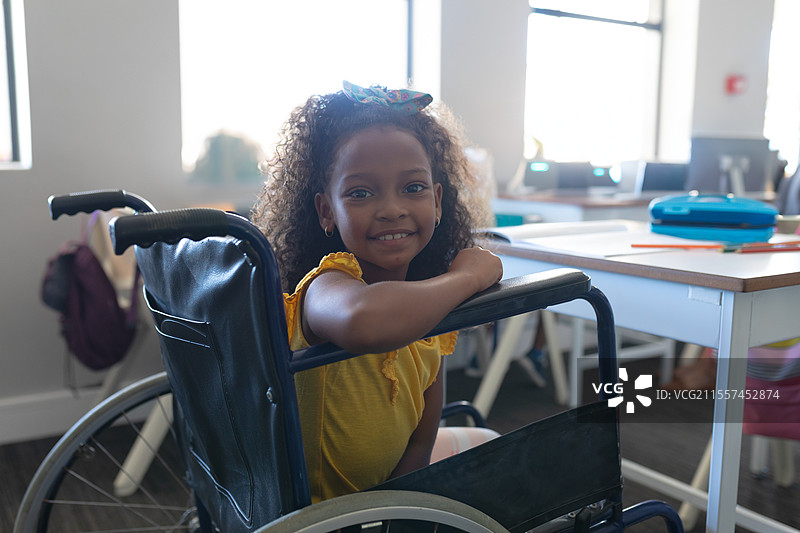 在学校，微笑的女孩坐在轮椅上参与课堂活动图片素材