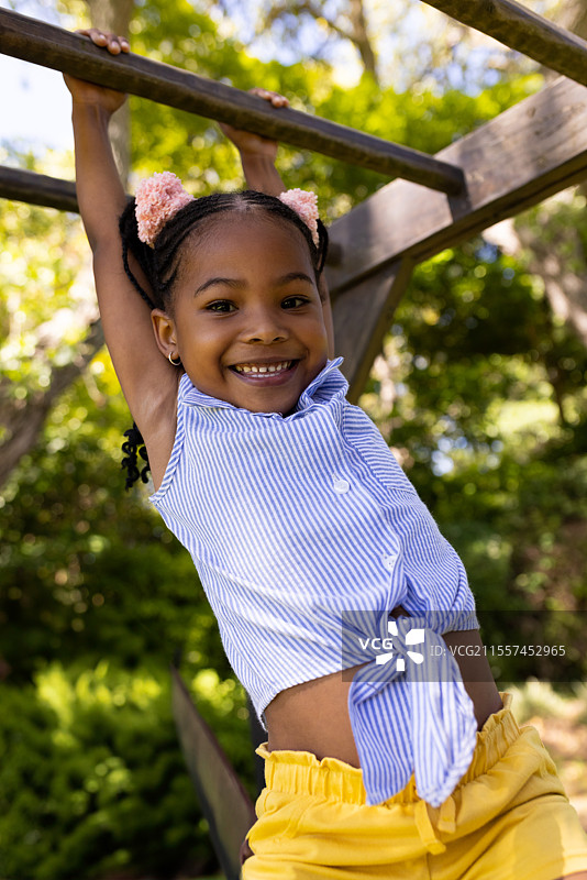 微笑的女孩在公园的单杠上玩耍，享受阳光明媚的户外时光图片素材
