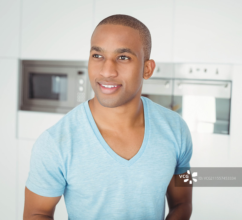 微笑的非裔美国男子穿着蓝色衬衫，在现代厨房中享受轻松时刻图片素材