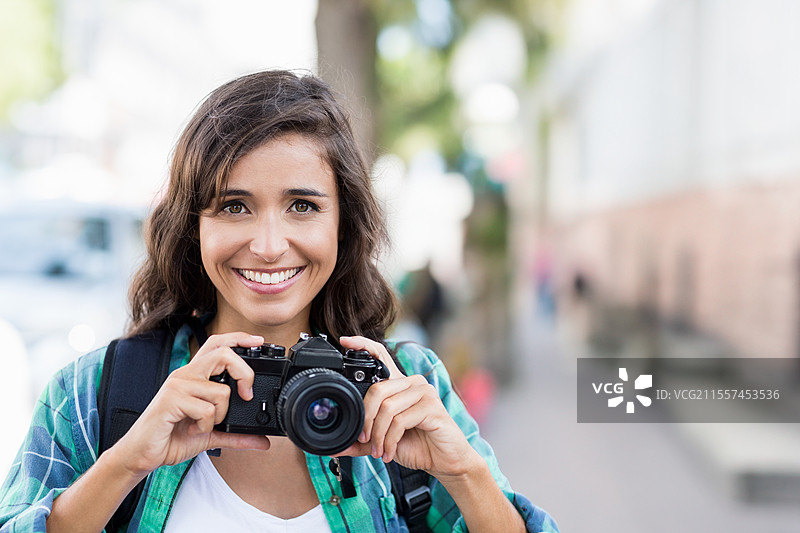 微笑的女性在城市街道上手持相机，享受城市摄影冒险，留白空间图片素材