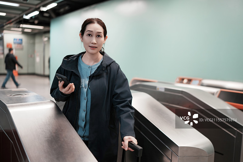 年轻女子手持智能手机在地铁旋转栅门上扫描图片素材