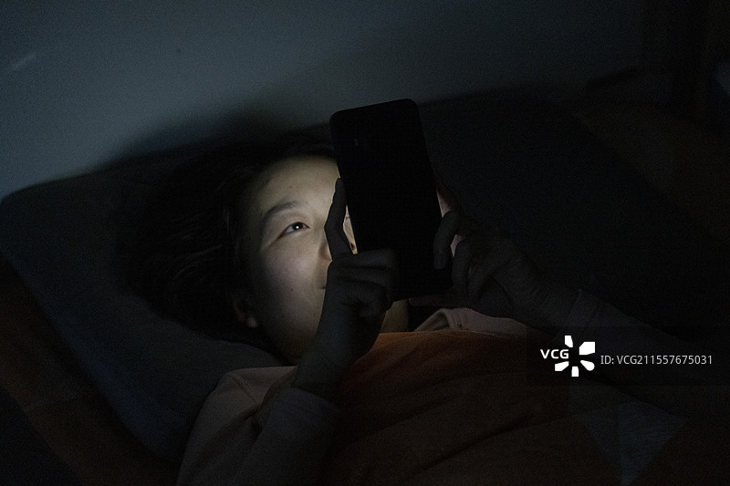 亚洲女士躺床看手机图片素材