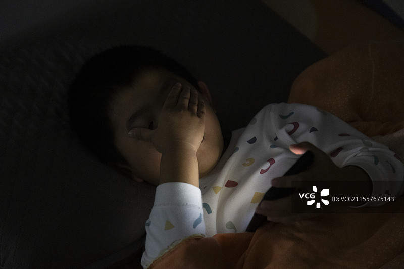 小朋友夜晚躺床看手机图片素材