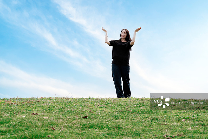 蓝天下草山上拥抱自然的快乐女人图片素材
