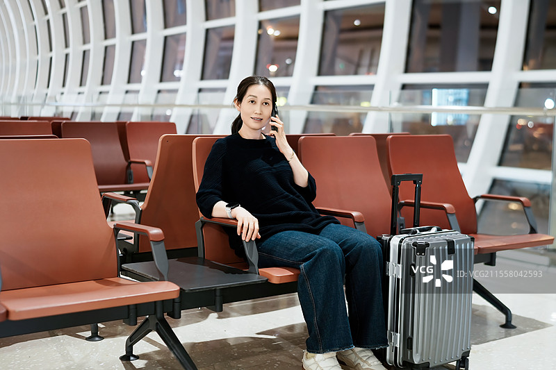 持行李和电话在机场候机室等候的妇女图片素材