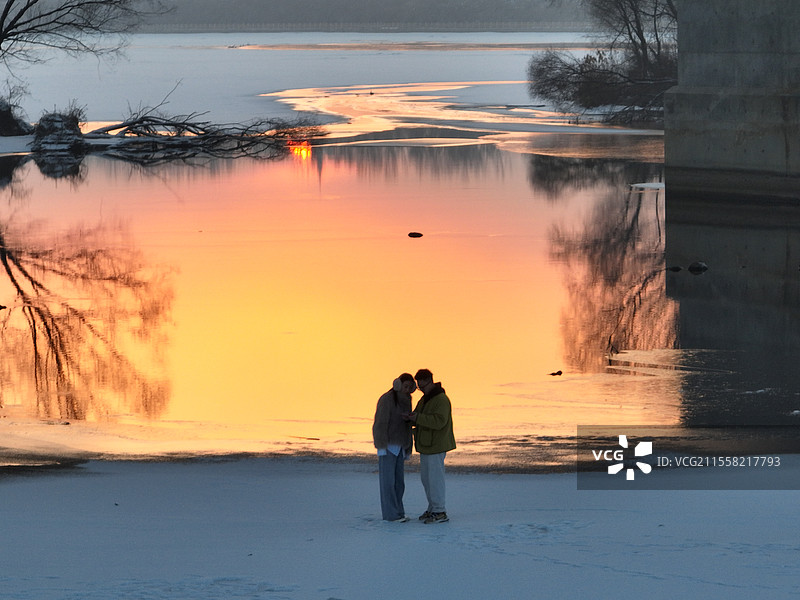 情侣在夕阳下的冬季河边图片素材