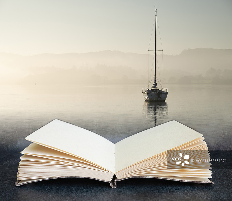 数字合成概念图，展示一本打开的书，书中有美丽的自然风光，静止的帆船停靠在湖区宁静的湖水中，背景是秋季晨雾中的平和日出。图片素材