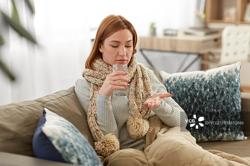 人们、健康与治疗的概念 - 悲伤的生病年轻女性在家中用水服药。生病的女性在家中用水服药。图片素材