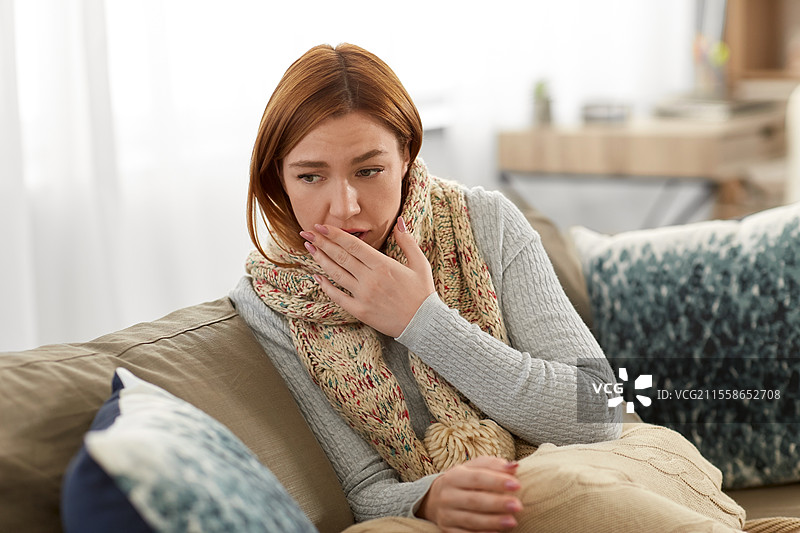 生病的女人裹着围巾和毯子在家咳嗽。图片素材