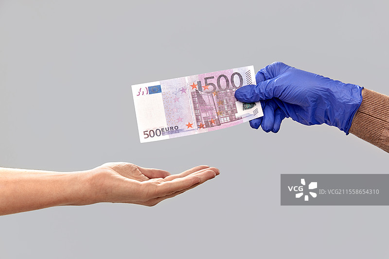 金融、支付和疫情概念 - 医用手套中的手在灰色背景上递出现金。图片素材
