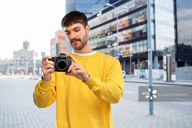 摄影与人们的概念 - 穿着黄色卫衣的年轻男性摄影师在城市背景下用数码相机拍照。年轻男子在城市中使用数码相机。图片素材