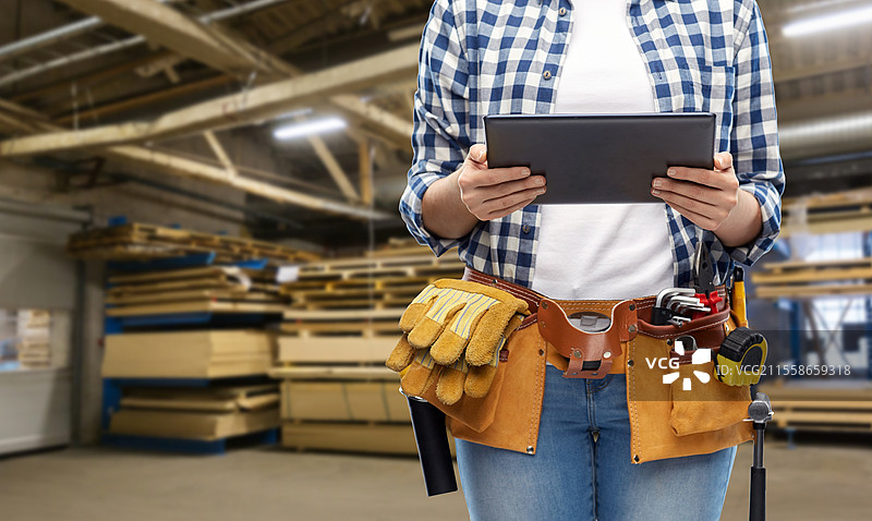 工业、生产和就业概念 - 背景为工厂车间的女性或工人特写，手持平板电脑，腰间挂着工具。女性或工人与平板电脑和工作工具。图片素材