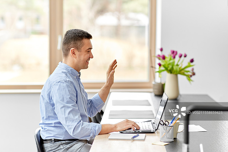 远程工作，商业与人际关系概念 - 开心微笑的中年男子在家办公室使用笔记本电脑进行视频通话。图片素材