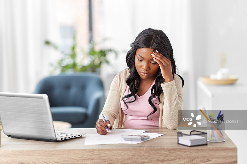 远程工作，科技与人文概念 - 年轻的非裔美国女性在家办公，手里拿着计算器和文件。图片素材