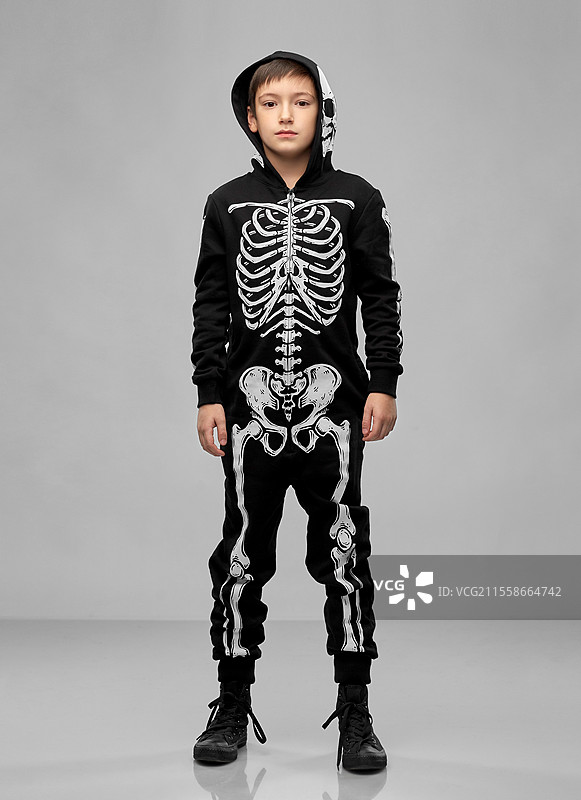 万圣节，节日和童年概念 - 穿着黑色服装、身上有骷髅骨的男孩，背景为灰色。穿着黑色万圣节服装的男孩，身上有骷髅骨。图片素材