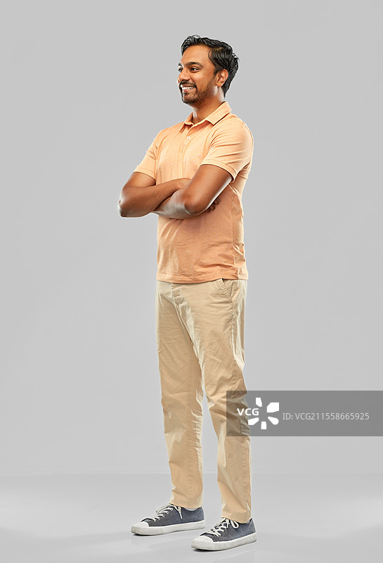 人和家具概念 - 一位年轻的印度男子微笑着，双臂交叉，背景为灰色。图片素材