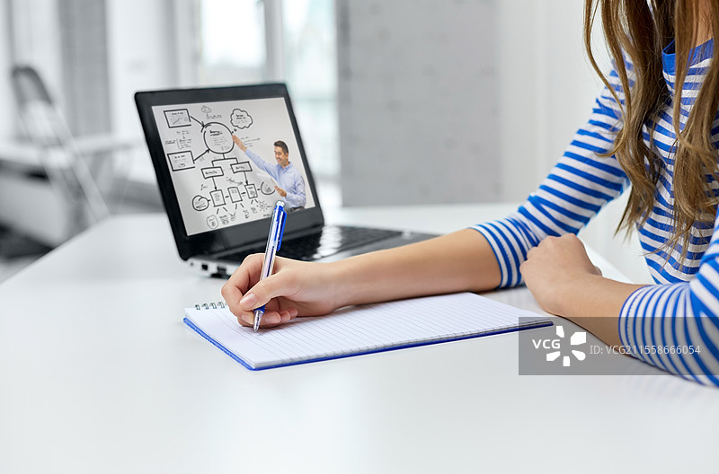 教育、电子学习和学校概念 - 学生女孩近距离使用练习本、钢笔和老师在笔记本电脑上进行在线课程的场景。学生女孩与练习本、钢笔和笔记本电脑。图片素材