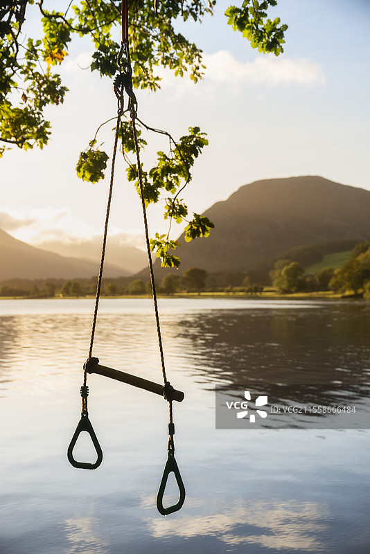 典型的英格兰夏季风景，孩子在湖区平静湖面上荡秋千，金色夏日的日出时分。图片素材