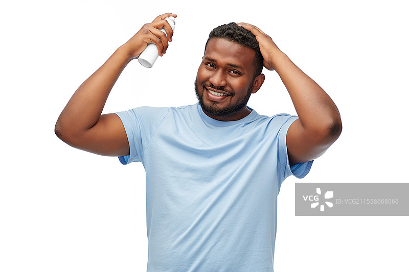 美容、发型设计和人们的概念 - 微笑的年轻非洲裔美国男子在白色背景下给头发喷发胶。非洲裔美国男子正在给头发喷发胶。图片素材