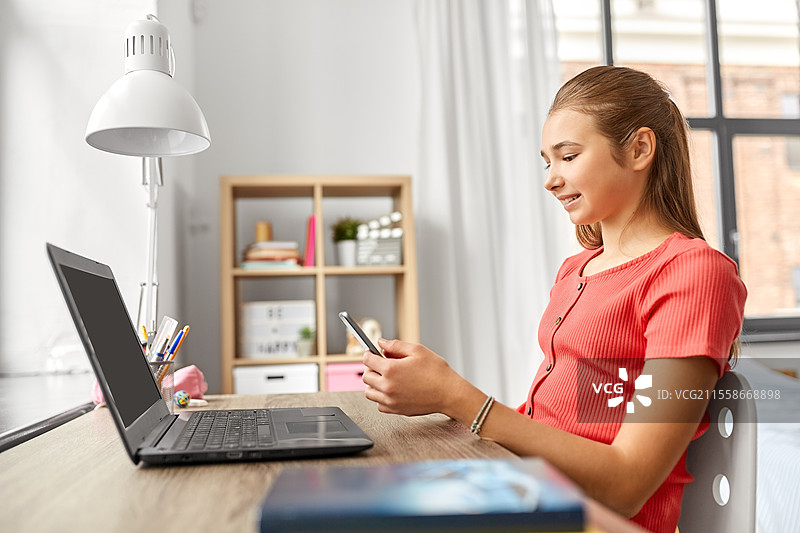 孩子们、科技与沟通的概念 - 开心微笑的少女学生在家中分心于作业，正在用智能手机发短信。女孩用智能手机分心于作业。图片素材