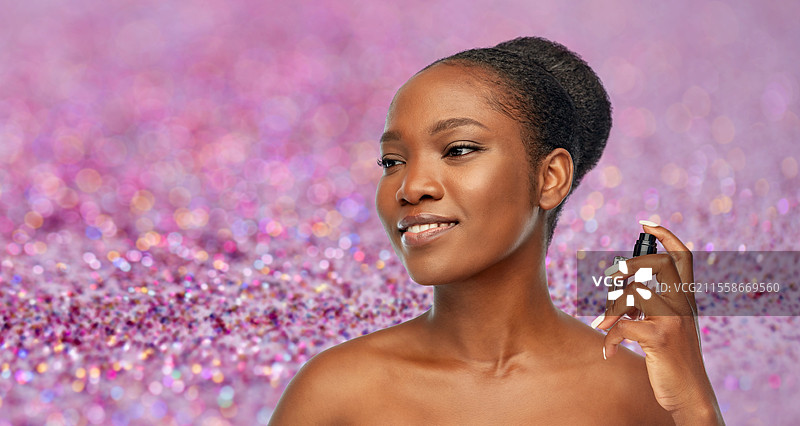 美丽、奢华和香水概念 - 一位快乐微笑的年轻非裔美国女性，肩膀，手持香水，背景是紫色闪光。年轻的非裔美国女性与香水。图片素材